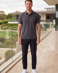 MOVE Sport Apparel Essential Polo Shirt. Man wearing the Heather Black polo on a modern clubhouse terrace.