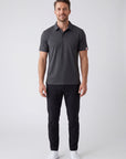 MOVE Sport Apparel Essential Polo Shirt. Man wearing the Heather Black polo, black trousers and white shoes in a neutral studio.