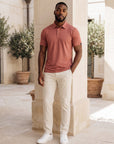 MOVE Sport Apparel Essential Polo Shirt. Man wearing the Mesa Rose polo with cream trousers in a limestone courtyard.