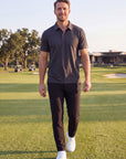 MOVE Sport Apparel Essential Polo Shirt. Man walking on a golf course wearing the Heather Black polo.