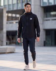 Man wearing the black MOVE Sport Apparel men’s AquaLight Packable Jacket in an urban outdoor setting.