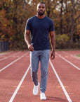Man warming up on an outdoor track in autumn wearing Blue Mirage MOVE Sport Apparel men’s Essential Jogger with a plain untucked navy tee and white trainers.
