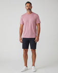 Full-body studio view of a man wearing MOVE Sport Apparel men’s Essential Short Sleeve in Heather Crimson with dark shorts and white trainers.
