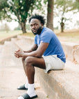 Side portrait of a man wearing a blue LuxDry Training T-Shirt on a park wall.