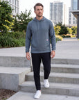Athletic male model walking down concrete steps in the MOVE Sport Apparel men’s waffle hoodie in Blue Heather Ashes, black training pants and white athletic shoes.