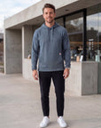 Athletic male model wearing the MOVE Sport Apparel men’s waffle hoodie in Blue Heather Ashes outside a modern cafe, with black training pants and white athletic shoes.