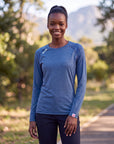 A woman wearing a MOVE sport apparel blue long sleeve shirt with a crew neck, standing outdoors in a park.