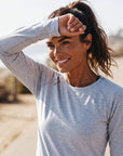 A woman wearing a MOVE sport apparel light grey long sleeve shirt with a small red logo on the cuff, outdoors.
