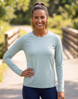 A woman wearing a MOVE sport apparel light green long sleeve shirt with raglan sleeves outdoors on a sunny path.