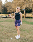 MOVE sport apparel woman wearing a black cropped tank top and purple athletic skirt on a golf course