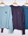 MOVE sport apparel Black Label crewneck sweatshirts in light blue, dark purple, and teal hanging on wooden hangers.