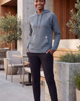 Female model wearing MOVE Sport Apparel women’s Balsam Green waffle hoodie beside a modern café terrace, with black pants and white sneakers.