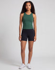 Front studio view of a woman wearing black MOVE Sport Apparel Women’s Biker Shorts with a short inseam, forest-green tank and white trainers.