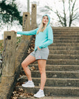 MOVE Sport Apparel women’s Black Label Lightweight Sun Hoodie: Woman wearing Aqua Splash sun hoodie and grey shorts beside outdoor stone stairs.