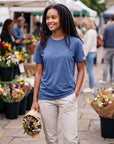 Woman wearing the Pageant blue MOVE Sport Apparel women’s Essential Short Sleeve T-shirt and light stone trousers at an outdoor flower market.