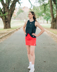 Woman wearing a coral-pink MOVE Sport Apparel women’s Skort with a black sleeveless top on a park path.