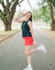 Woman wearing a coral-pink skort during a standing stretch on a tree-lined park path.