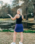 Woman wearing a purple MOVE Sport Apparel women’s Skort with a black sleeveless top on a golf course.