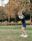 Woman wearing a purple MOVE Sport Apparel women’s Skort while swinging a golf club.