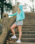 MOVE Sport Apparel women’s Black Label Lightweight Sun Hoodie: Closer view of Aqua Splash sun hoodie and grey shorts on outdoor stone stairs.