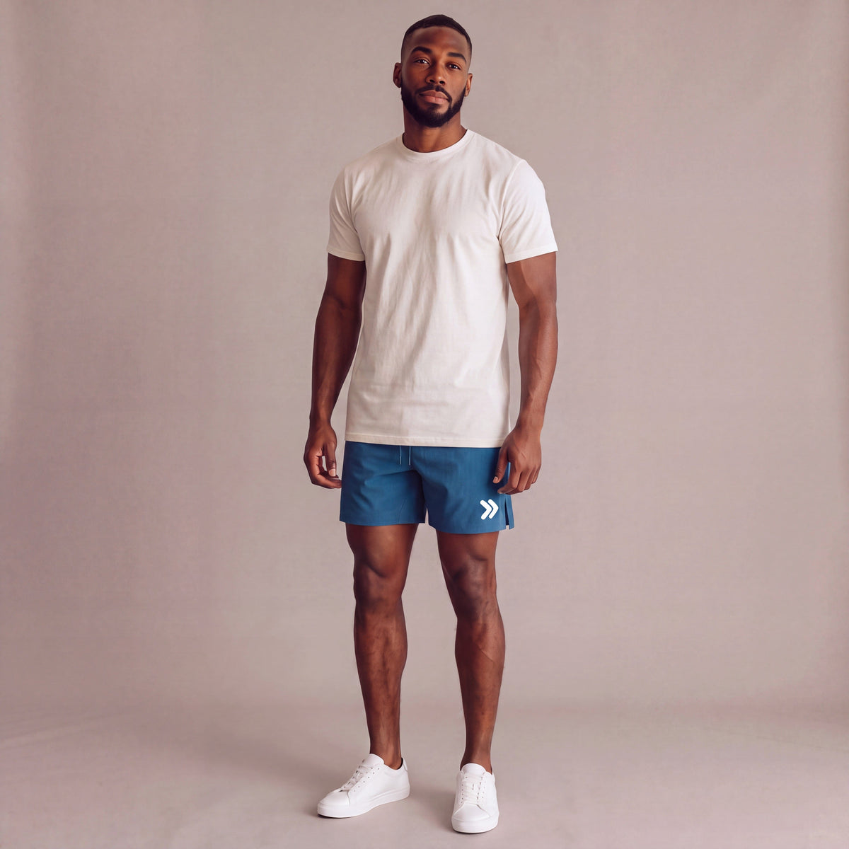 Male model wearing Mallard Blue MOVE Sport Apparel Agility 6 inch Training Shorts with a naturally untucked ivory tee in a neutral studio; original white thigh embellishment retained.