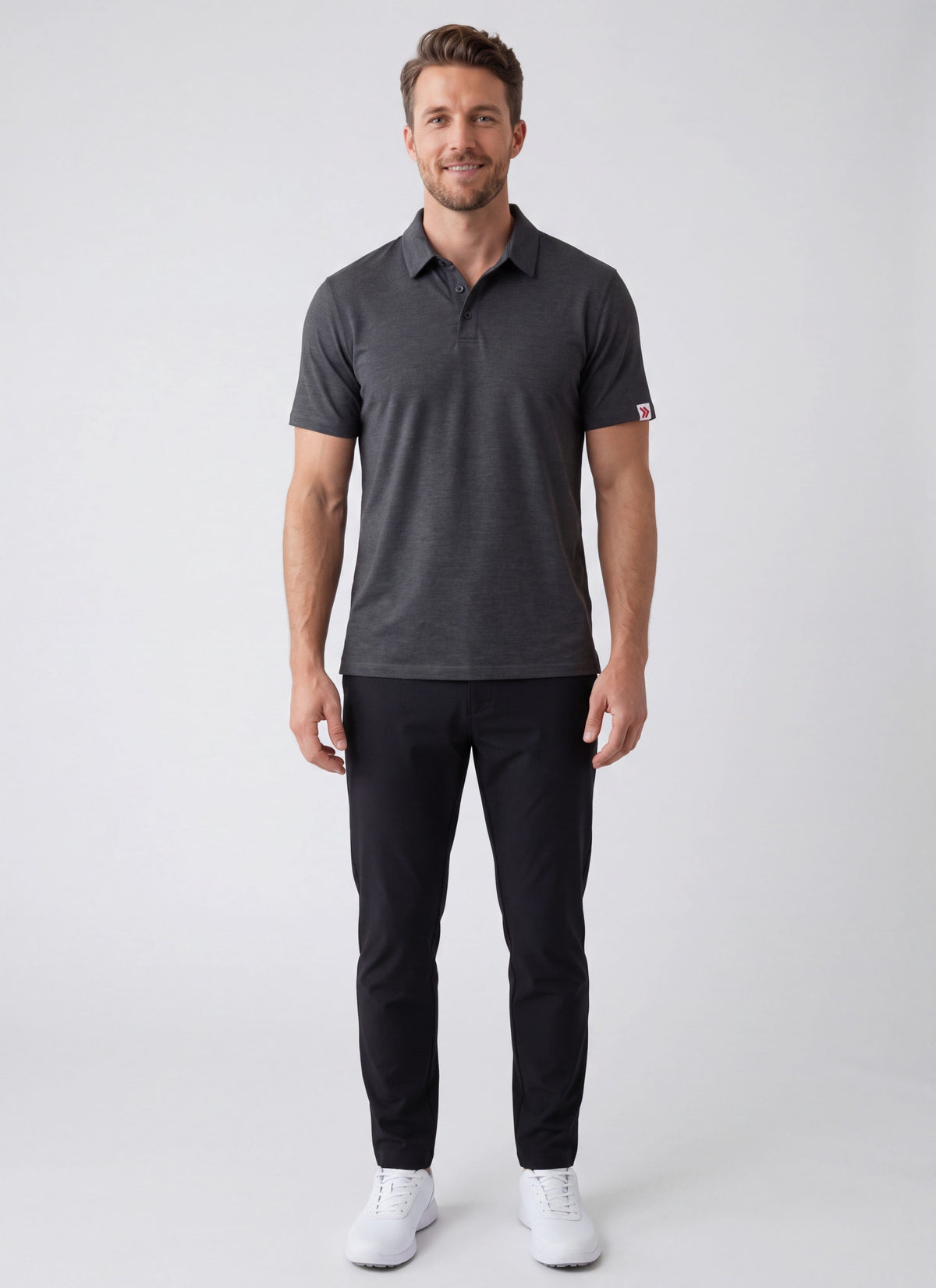 MOVE Sport Apparel Essential Polo Shirt. Man wearing the Heather Black polo, black trousers and white shoes in a neutral studio.
