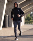Man running on an outdoor concrete path in the black MOVE Sport Apparel men’s AquaLight hooded jacket.