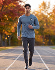 Man warming up on an outdoor track in autumn wearing MOVE Sport Apparel men’s Blue Mirage Black Label long sleeve top and plain charcoal running joggers; original black-and-white chest embellishment retained.