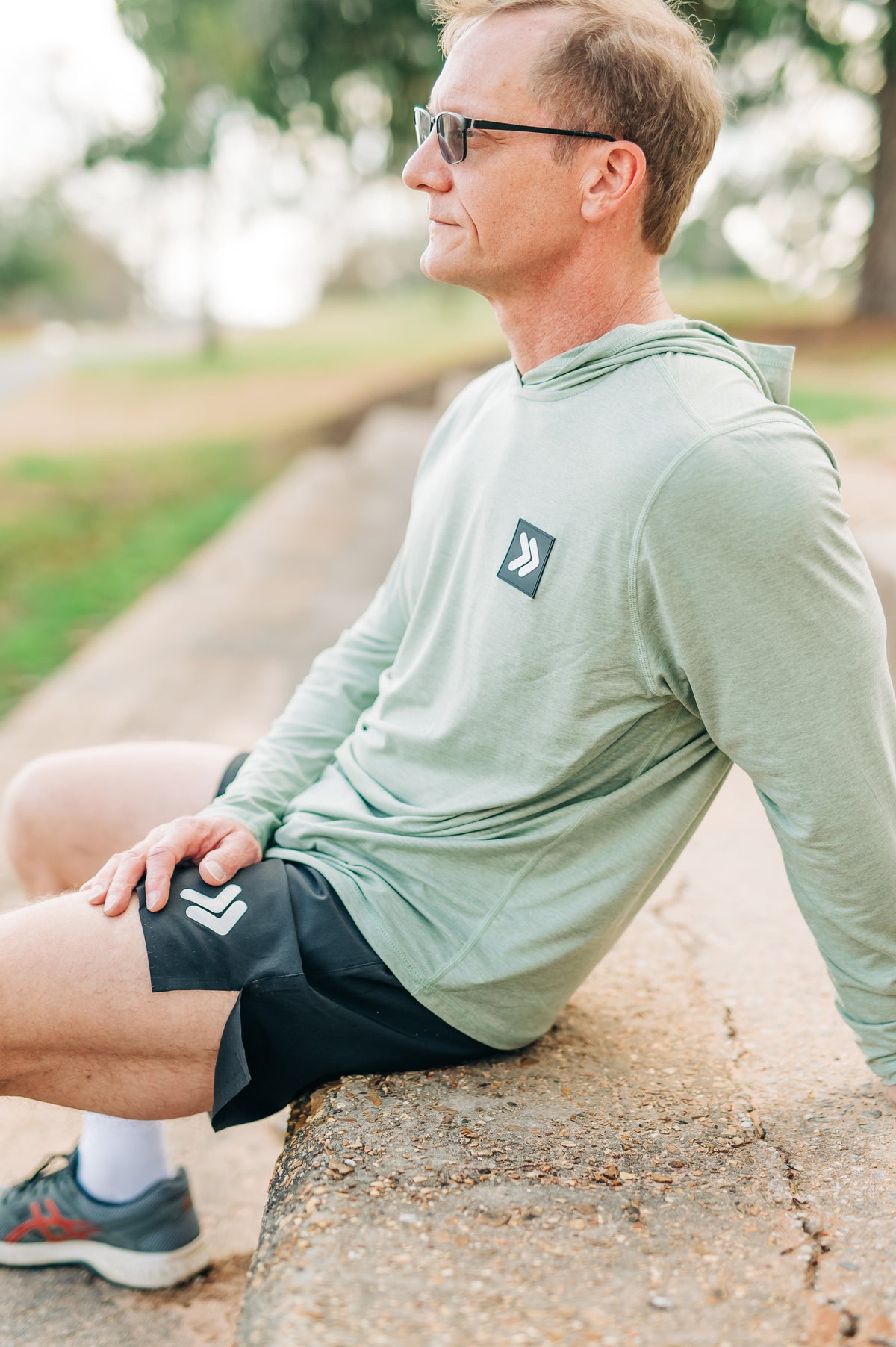 Man wearing the Seagrass MOVE Sport Apparel men’s Essential Lightweight Sun Hoodie and black shorts seated outdoors.