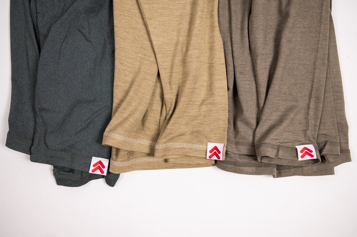 Close view of the original red-and-white cuff labels on three colors of MOVE Sport Apparel Men’s Essential Long Sleeve.