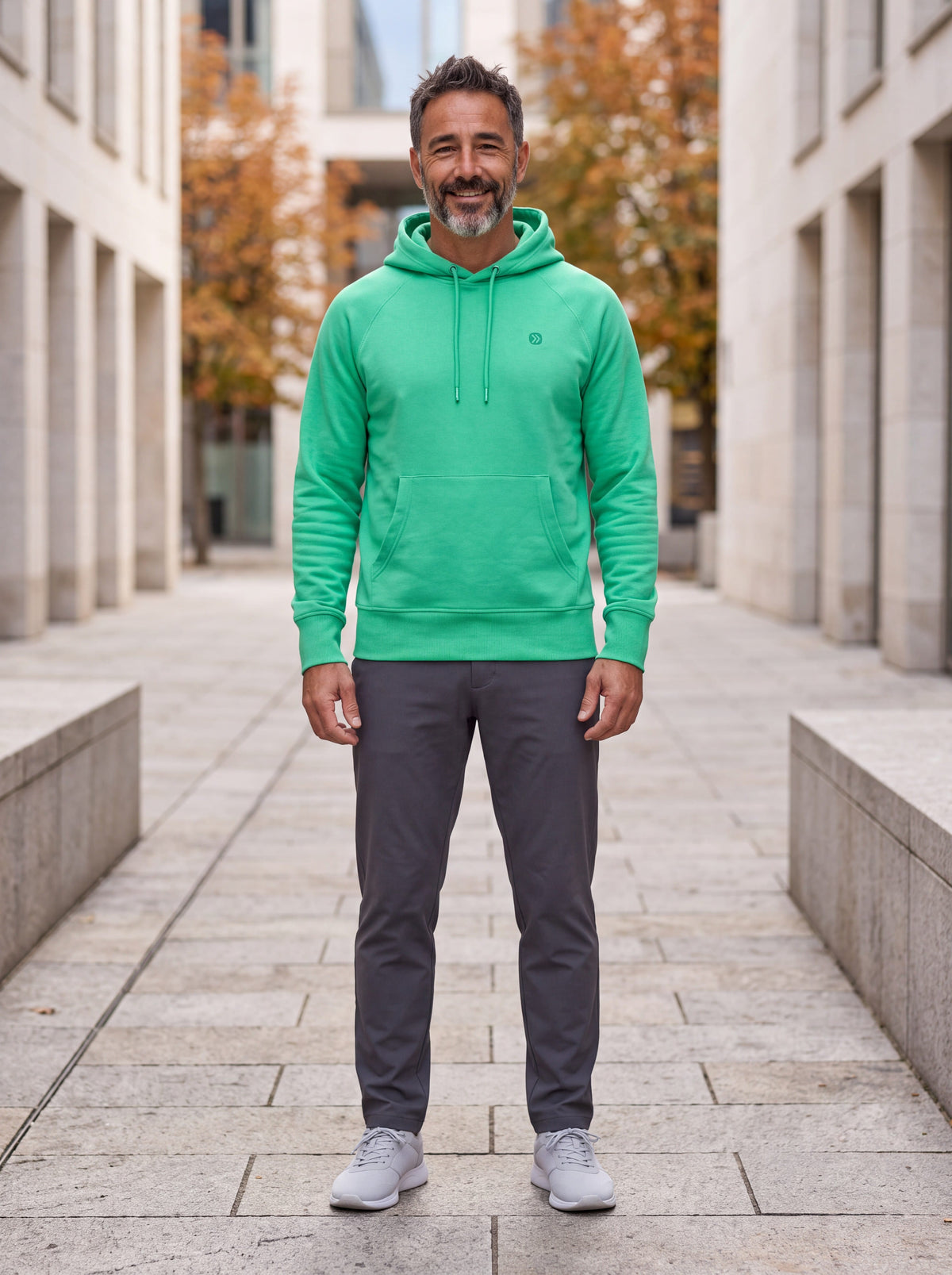 MOVE Sport Apparel men’s Essential Pullover Hoodie in Blarney green, worn by a smiling man standing on an autumn city walkway.