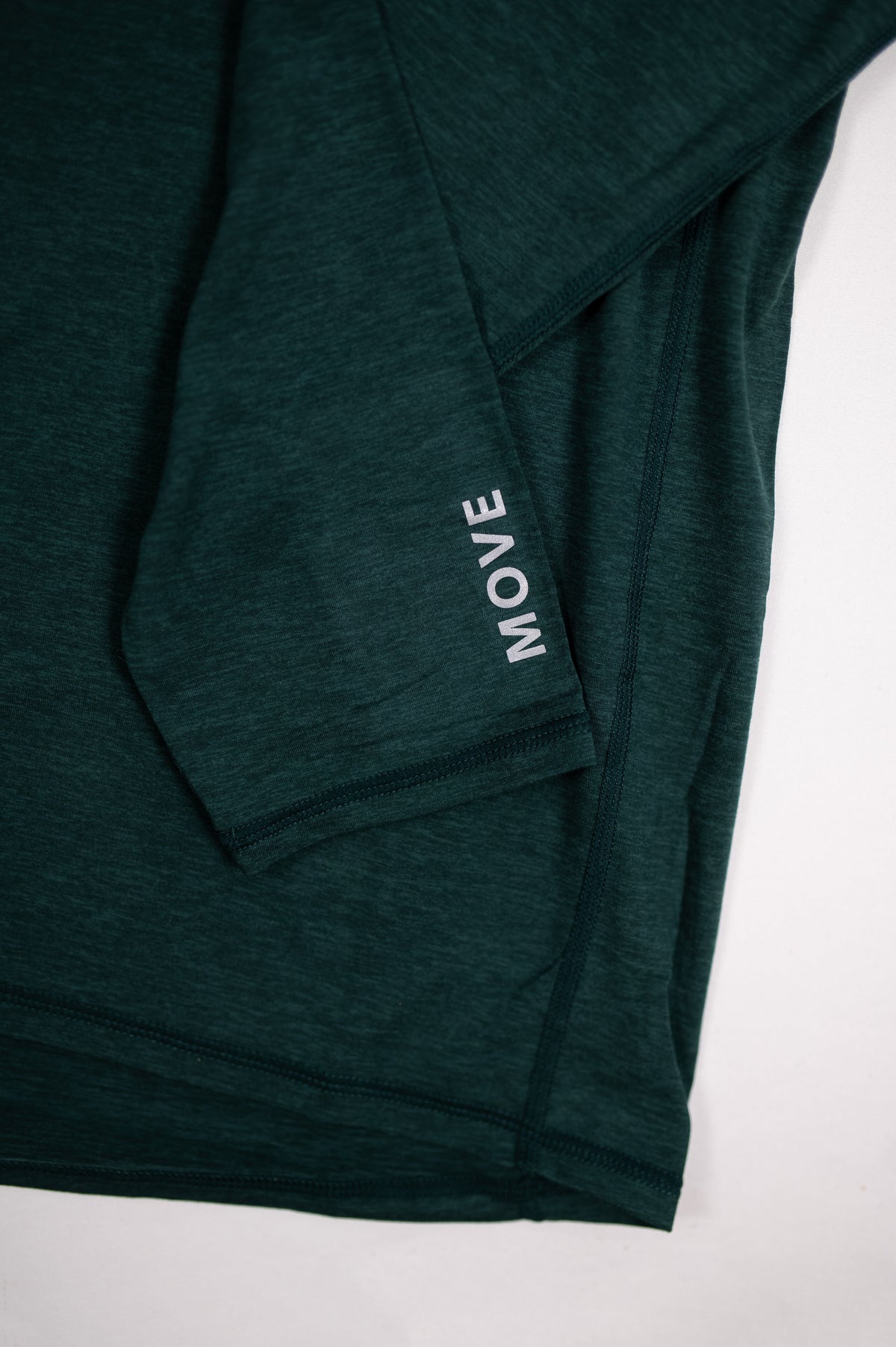 Close view of the original white MOVE forearm lettering on the MOVE Sport Apparel Men’s Essential Quarter Zip in Pine Grove.