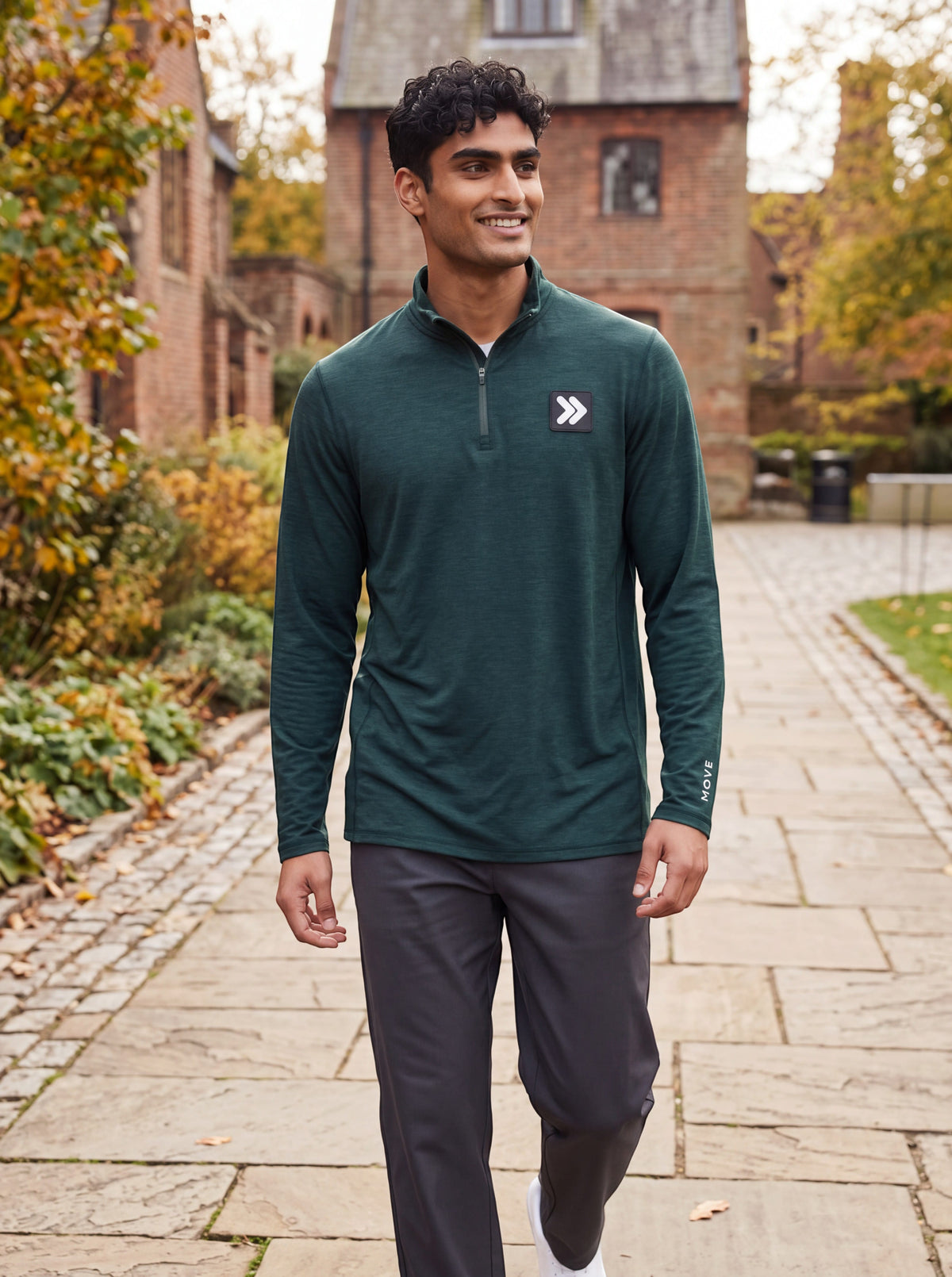 Man wearing MOVE Sport Apparel men’s Essential Quarter Zip in Pine Grove in a brick courtyard with autumn foliage.
