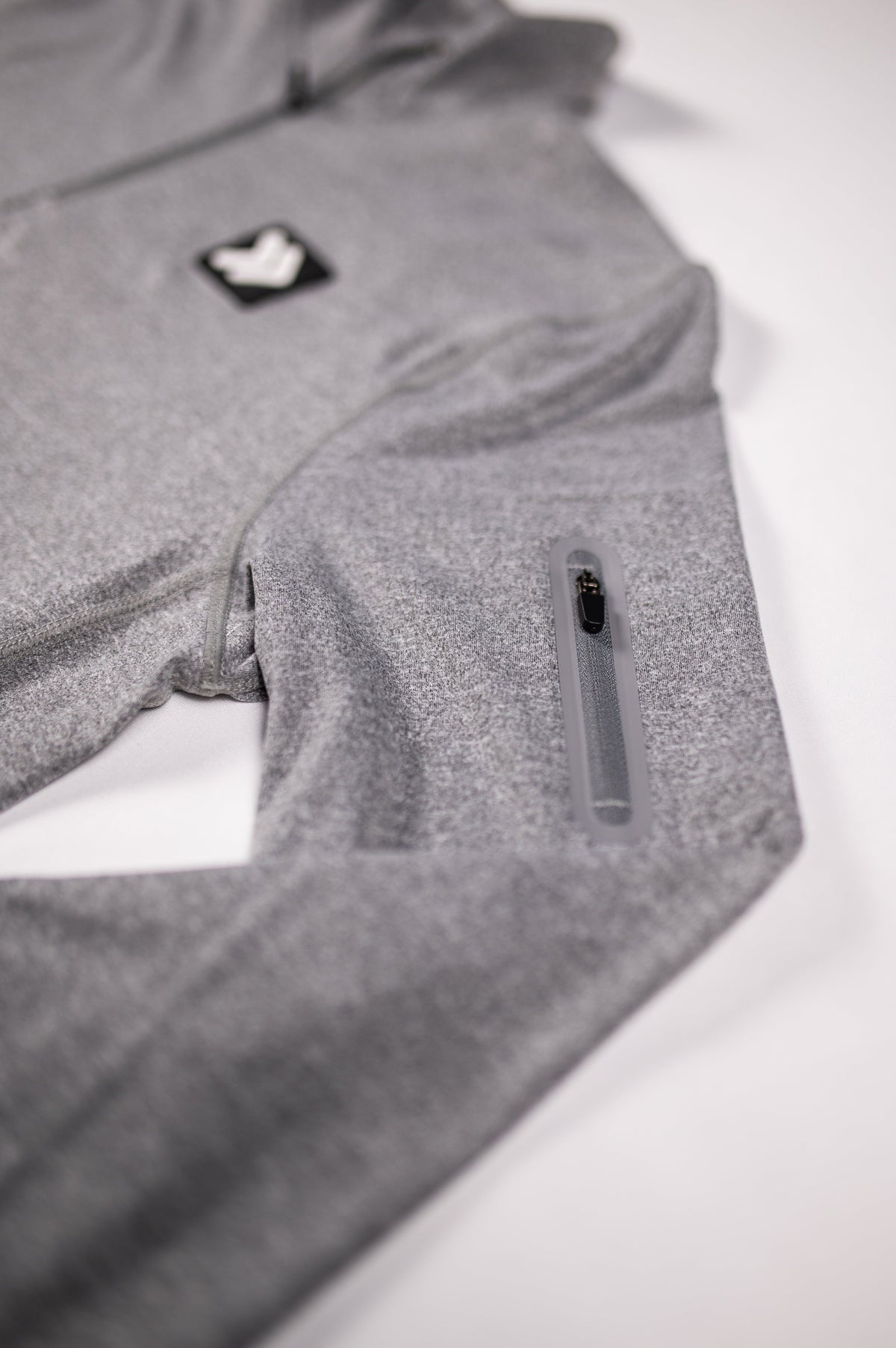 Close view of the Heather Classic Gray Essential Quarter Zip Pro original chest patch, heather fabric and zippered sleeve pocket.