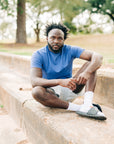 Front portrait of a man sitting outdoors wearing a blue LuxDry tee and light shorts.