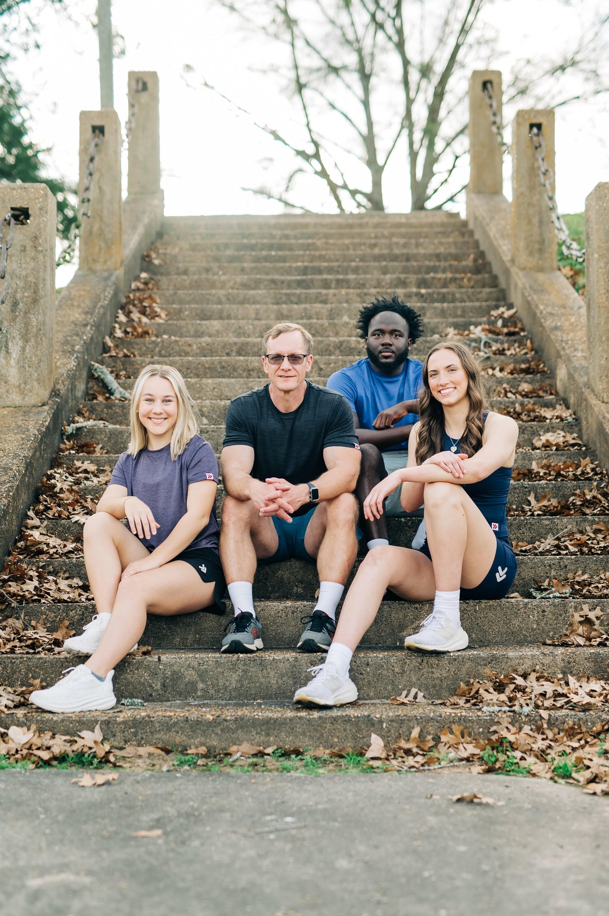 Group wearing MOVE Sport Apparel athletic outfits while seated on park steps, including a blue LuxDry tee.