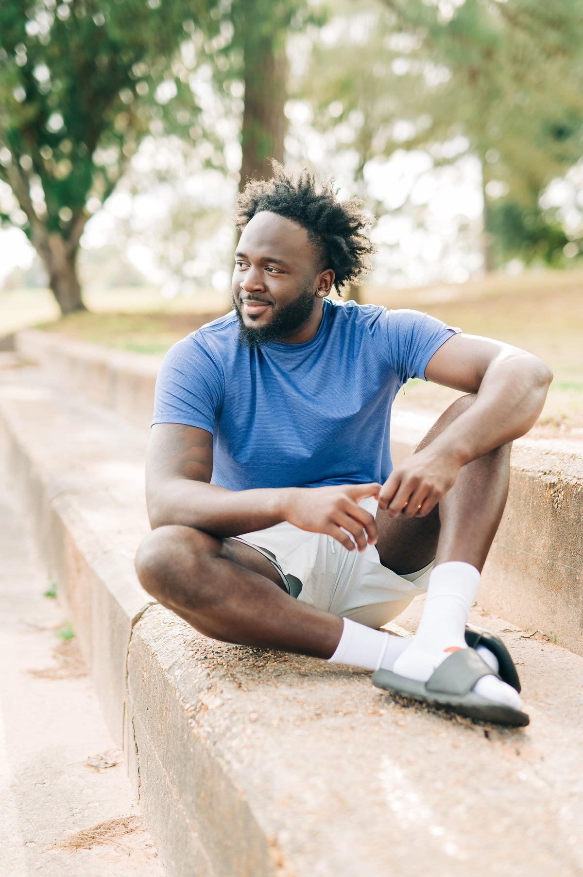 Man sitting in a relaxed pose outdoors wearing a blue LuxDry tee and light shorts.