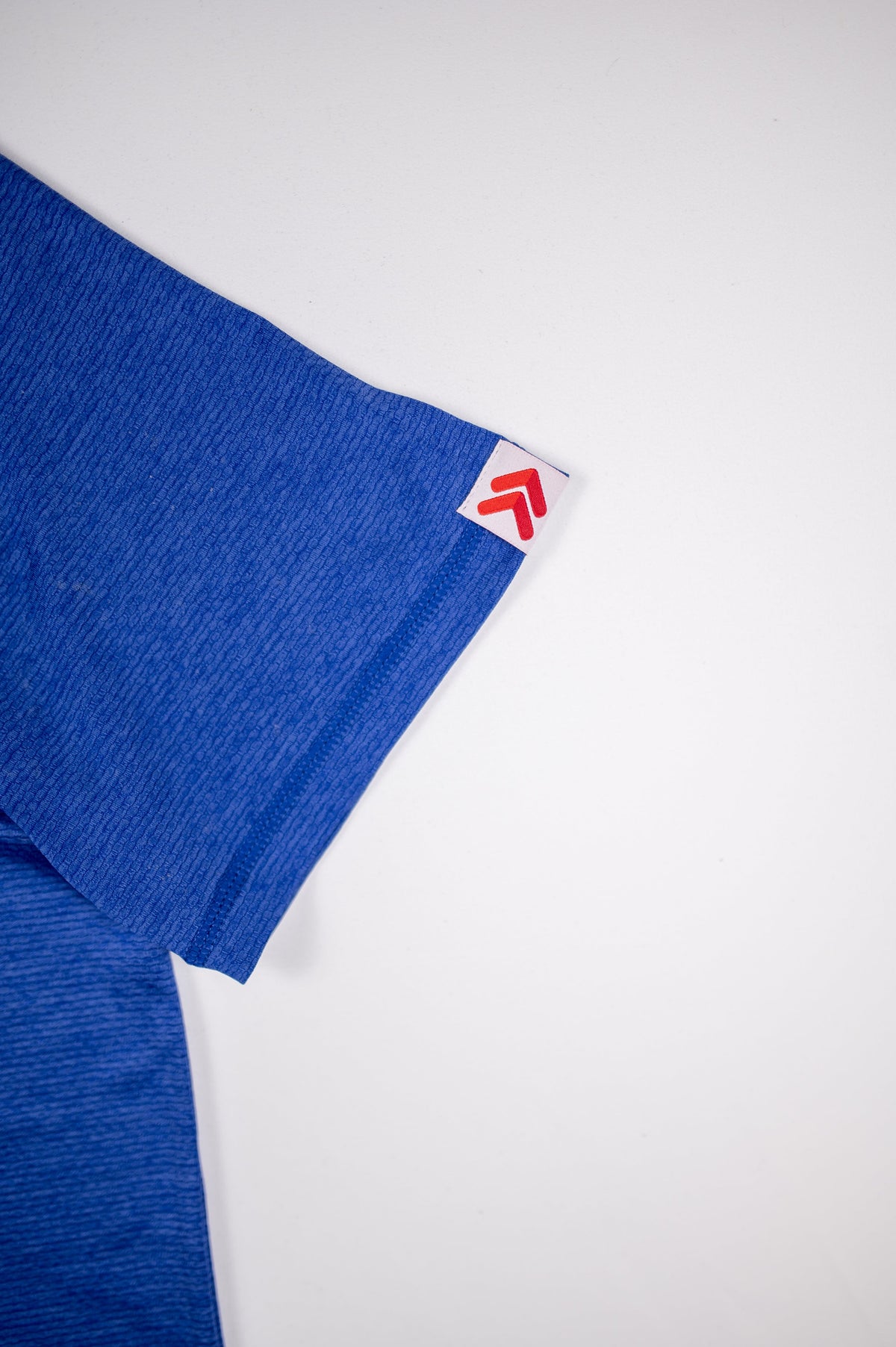 Surf the Web blue LuxDry tee sleeve hem showing original white tab and red double chevrons.