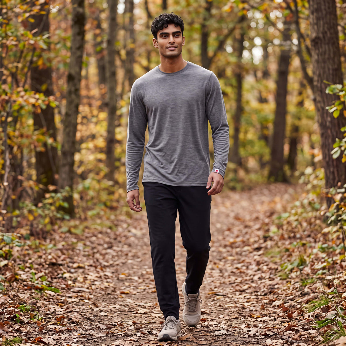 Man walking along an autumn woodland trail in the MOVE Sport Apparel Men’s Merino Long Sleeve in Granite Gray, showing the original red-and-white cuff label.