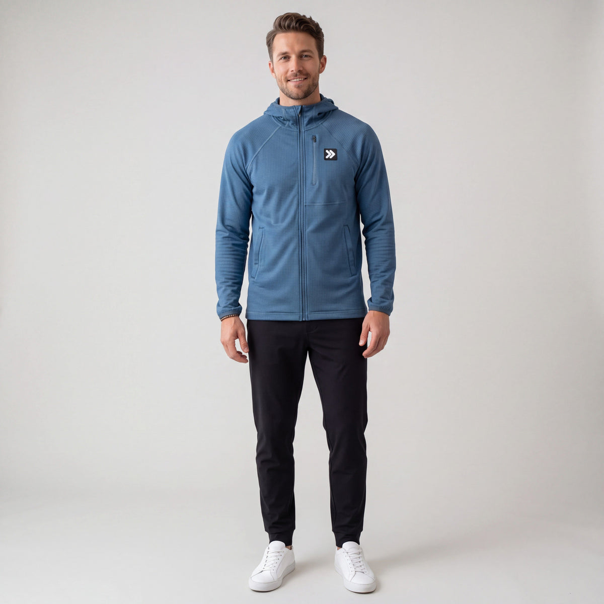 Full-body studio model wearing the MOVE Sport Apparel men’s waffle hooded jacket in Blue Mirage with black training pants and white sneakers.