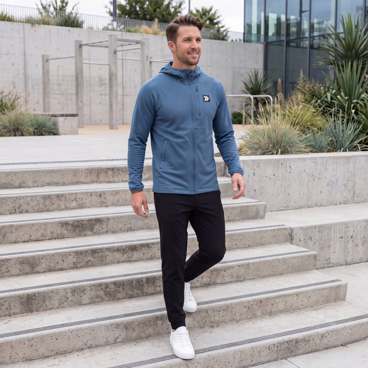 Man walking down concrete steps in the MOVE Sport Apparel men’s Blue Mirage waffle hooded jacket with black training pants.