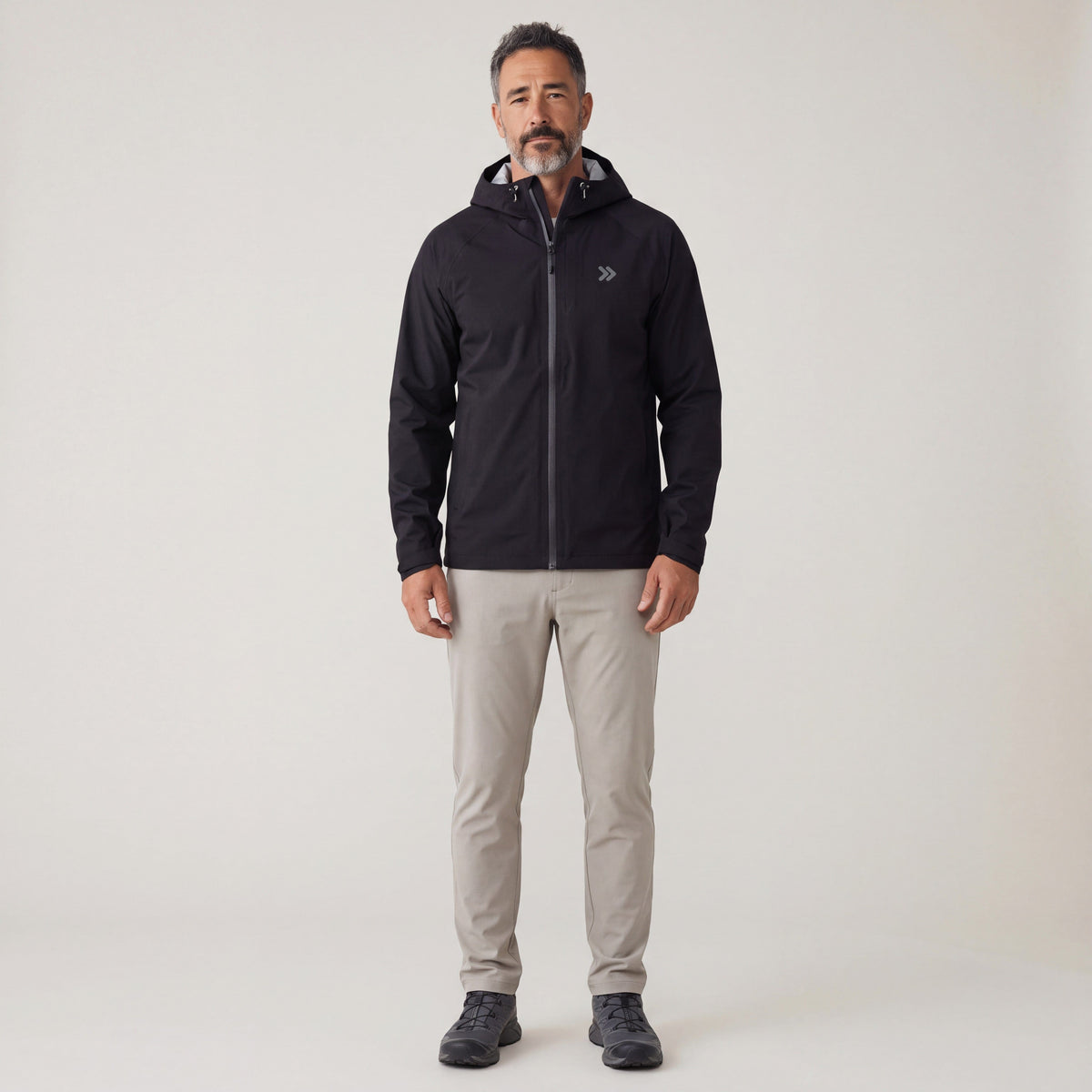 Full-length studio view of a man wearing the black MOVE Sport Apparel waterproof jacket with a gray chest embellishment.