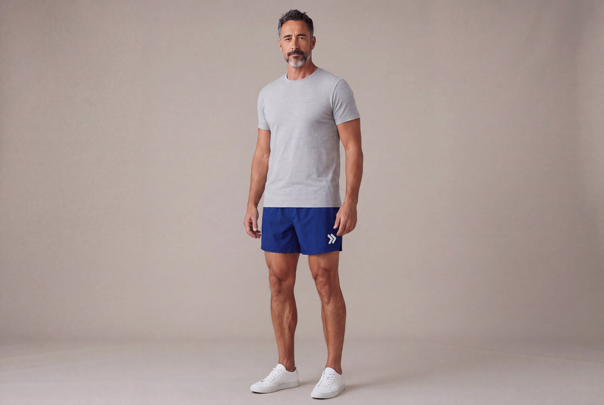Male model wearing Beacon Blue MOVE Sport Apparel men’s Performance 5 Inch Running Shorts with an untucked light-grey athletic T-shirt in a neutral studio; original white thigh embellishment retained.