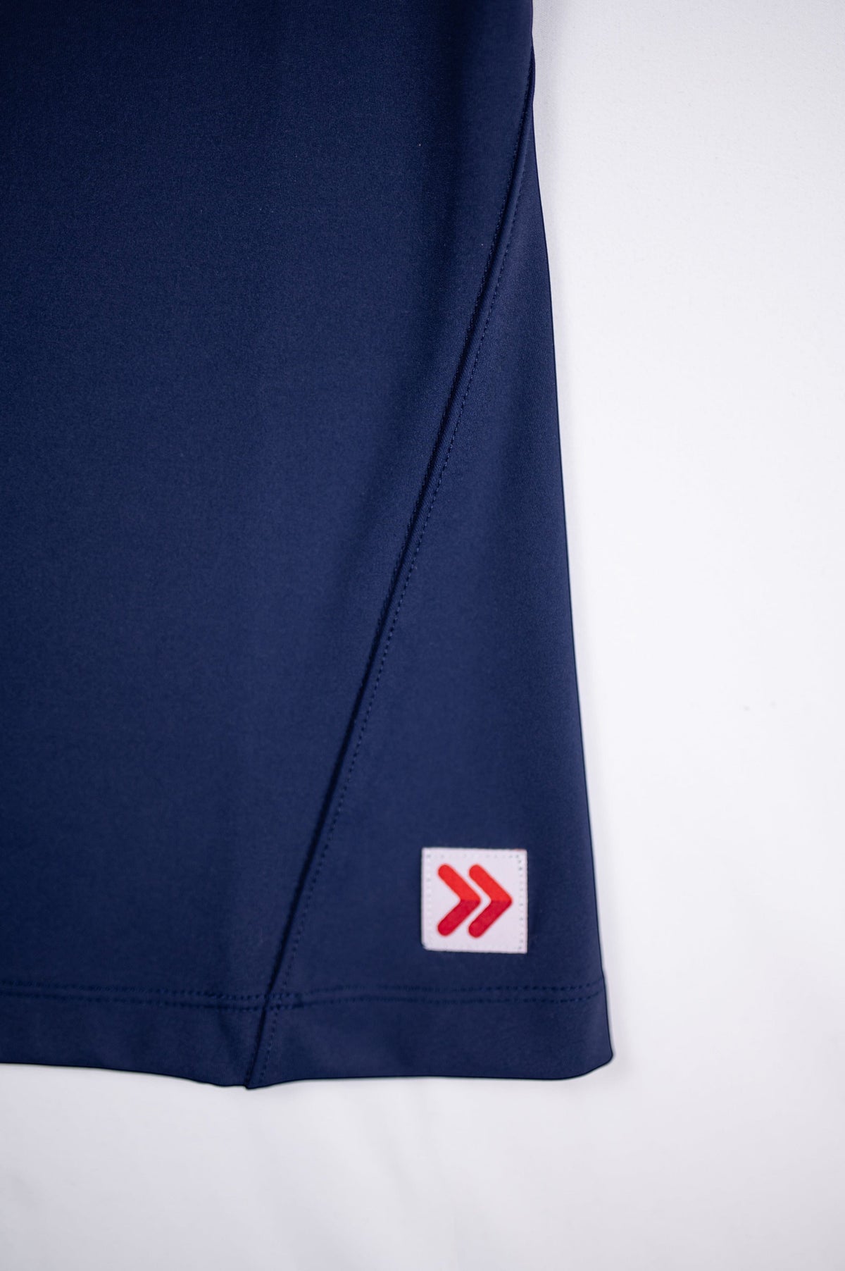 Close view of the original red-and-white hem tab on the Maritime Blue MOVE Sport Apparel Pure Stretch Full Length Tank Top.