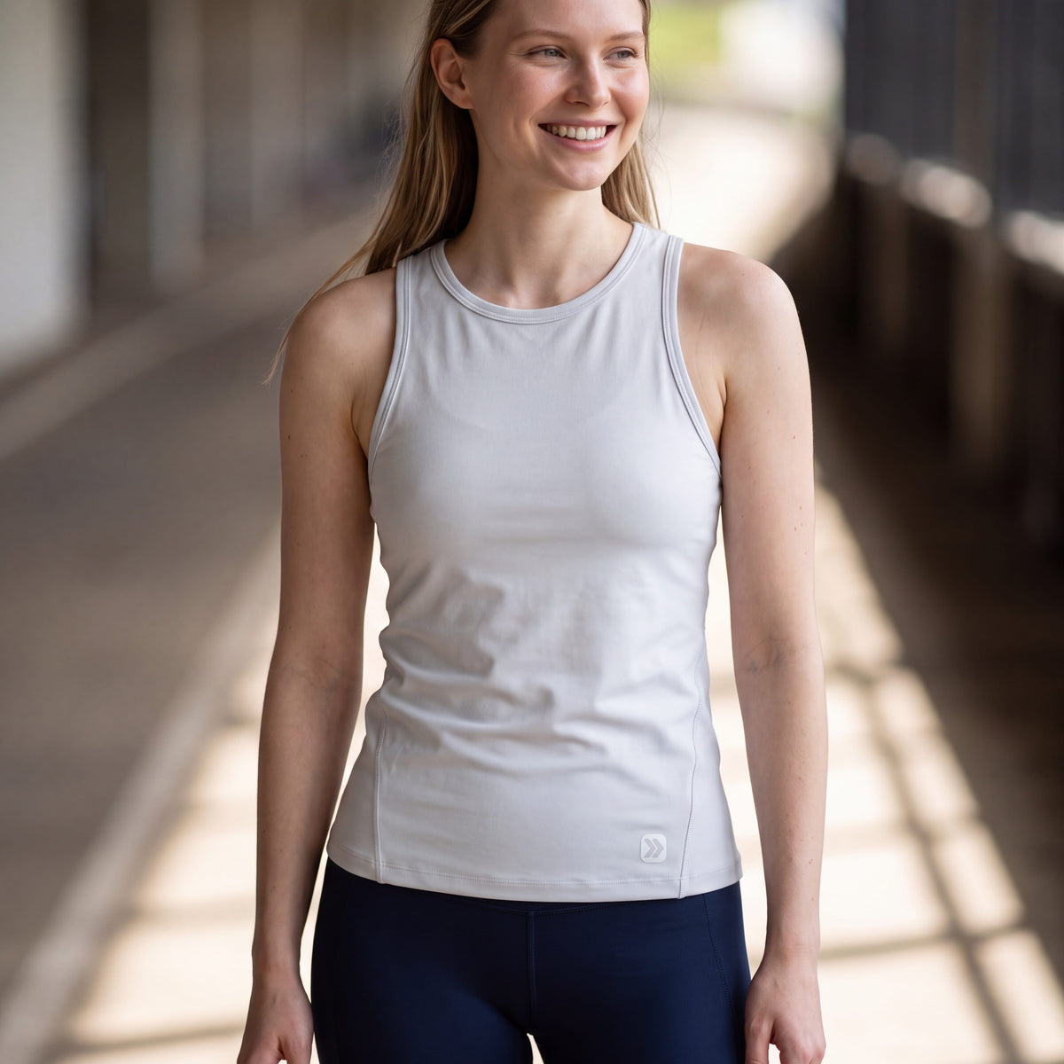 Woman wearing MOVE Sport Apparel Pure Stretch Full Length Tank Top in White beside a sunlit walkway.