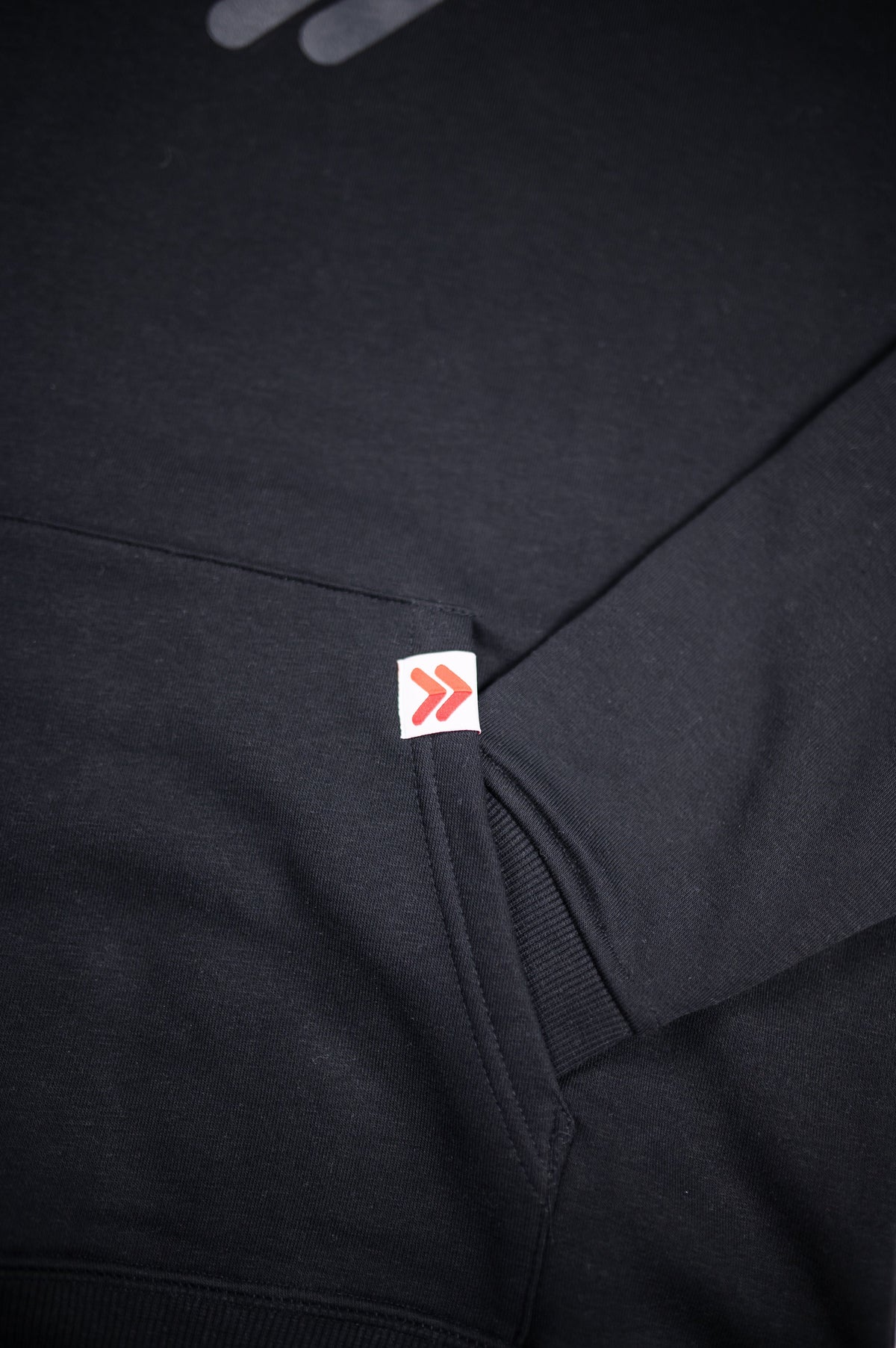 Close-up of the original red-and-white cuff embellishment on the black MOVE Sport Apparel Logo Hoodie.
