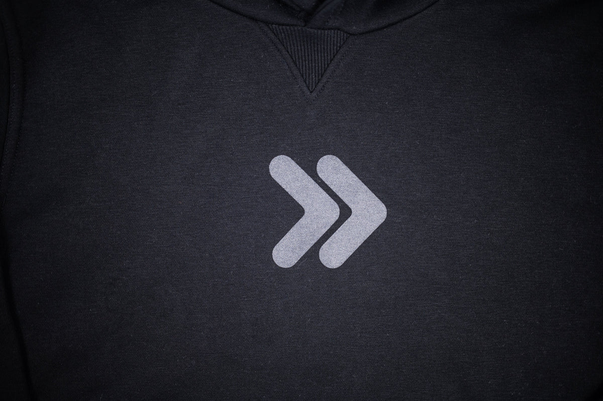 Close-up of the original grey centered double-chevron embellishment on the black MOVE Sport Apparel Logo Hoodie.