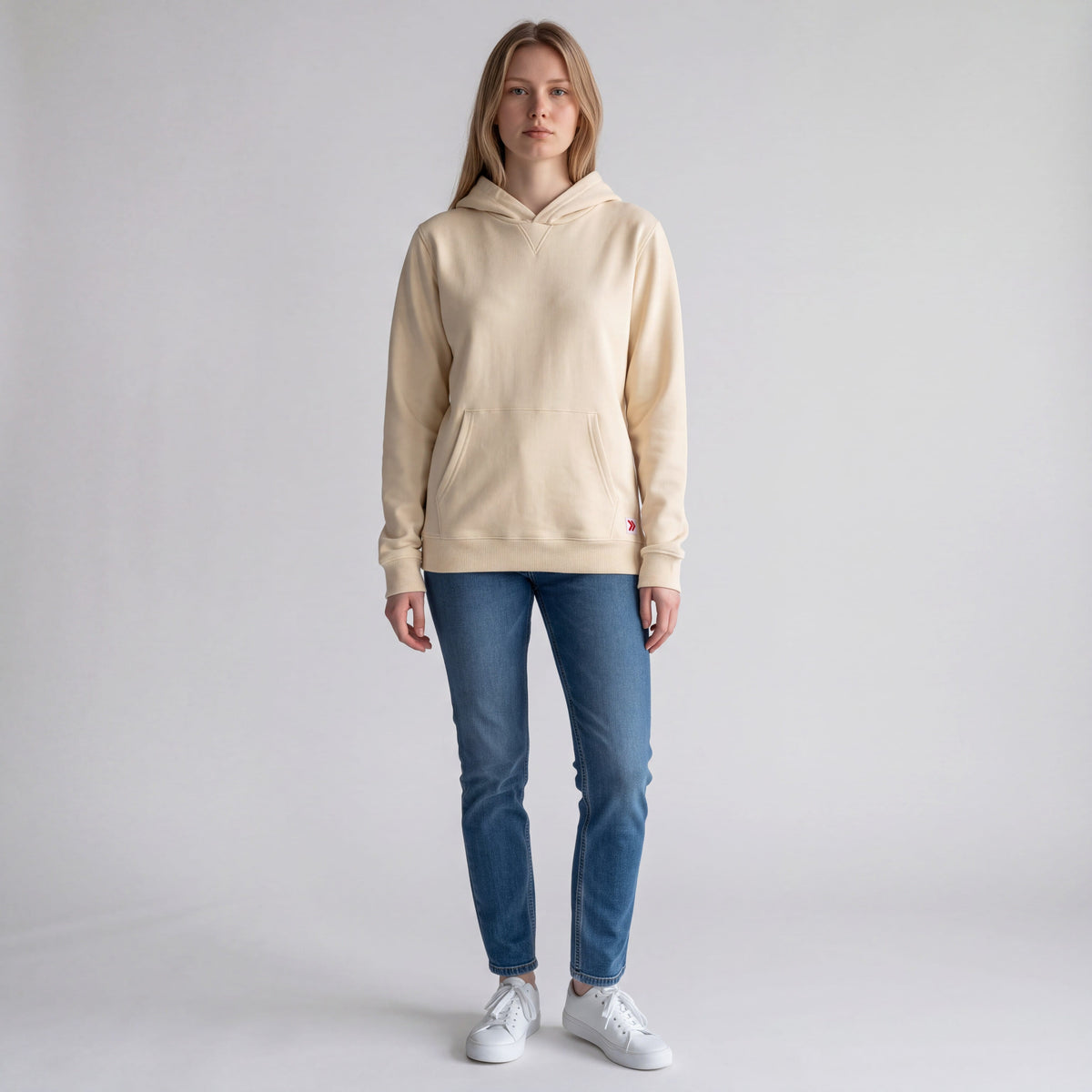 Full body studio view of a woman wearing the MOVE Sport Apparel French Terry Hoodie in Natural with blue jeans and white sneakers.
