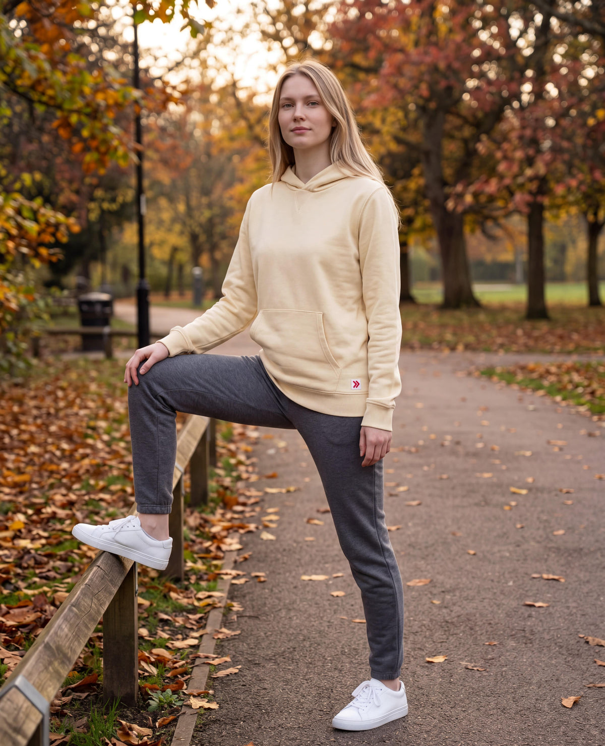 Woman stretching beside a wooden rail in an autumn park in the MOVE Sport Apparel French Terry Hoodie in Natural.