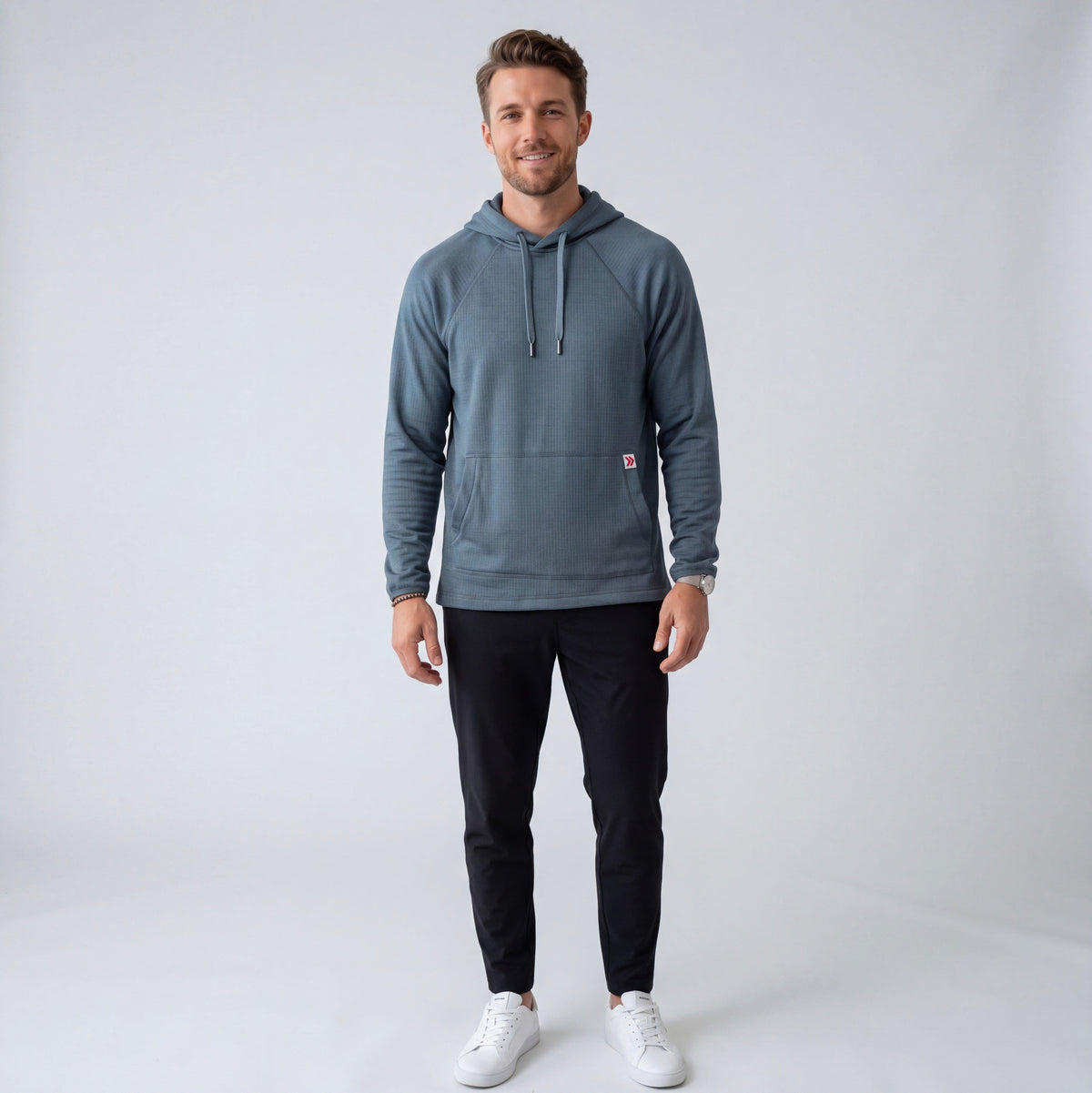 Full-body studio view of an athletic male model wearing the MOVE Sport Apparel men’s waffle hoodie in Blue Heather Ashes with black training pants and white athletic shoes.